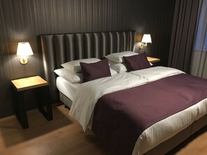 Une chambre d’hôtel moderne avec un grand lit, deux tables de chevet et une tête de lit.