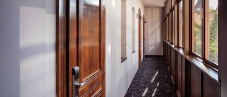 A hallway with wooden doors, arched windows, and a marble floor.