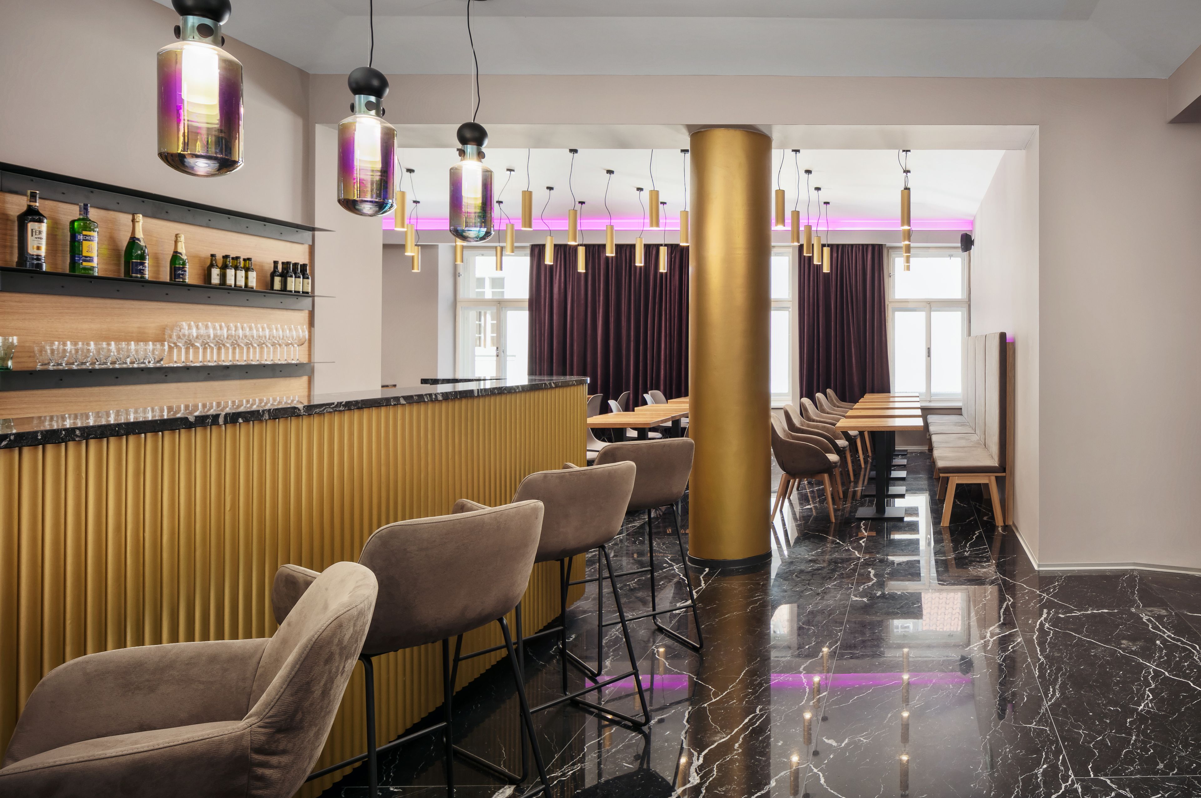 A modern bar area with a marble floor, bar stools, and a variety of bottles and glasses on shelves.