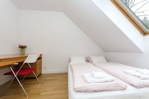 Un dormitorio con techo inclinado, un escritorio, una silla y dos camas con ropa de cama rosa.