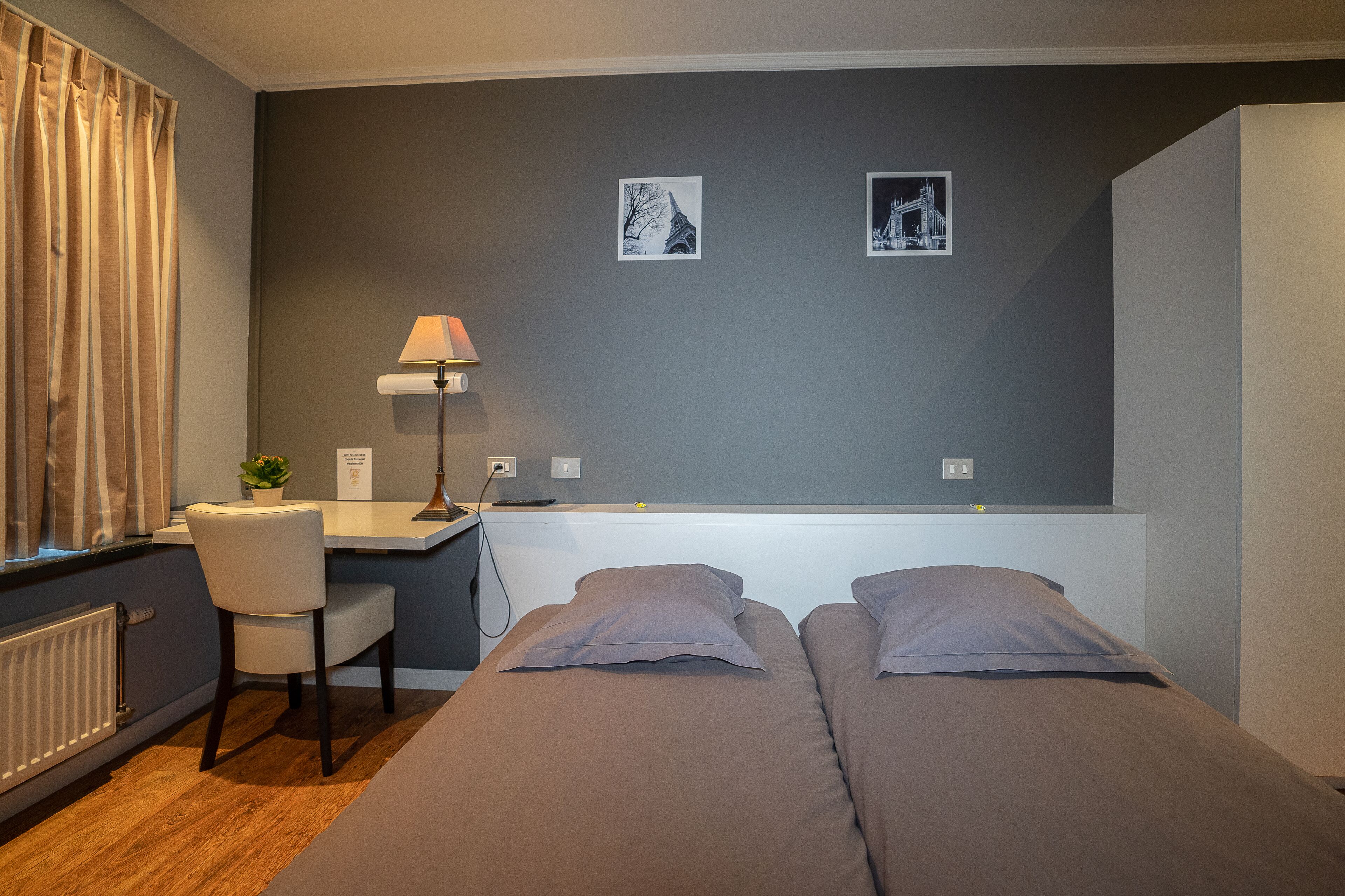Habitación de hotel con dos camas, un escritorio, una silla, una lámpara y dos cuadros en la pared.