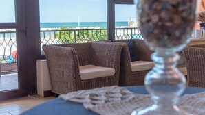 A wicker sofa with cushions, a glass table with a napkin, and a view of the sea through a window. - Hotel Giorgetti Orange (Bellaria-Igea Marina)