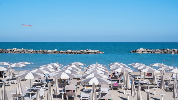 A beach with rows of umbrellas and lounge chairs, a clear sky, and a calm sea. - Hotel Giorgetti Orange (Bellaria-Igea Marina)