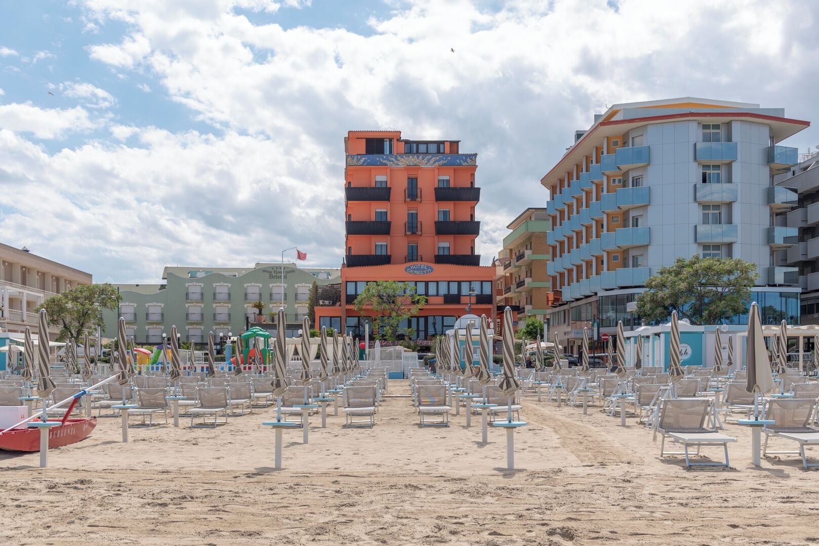 Un hotel frente a la playa con varios pisos, terraza al aire libre y una zona de arena.