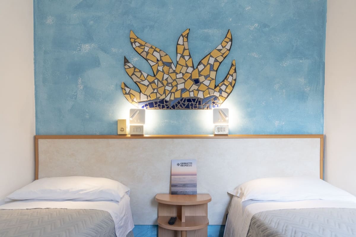 Camera d'albergo con due letti, un elemento decorativo a parete, un tavolino con un telecomando e una targa appesa al muro.