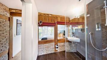A modern bathroom with a glass shower enclosure, a wooden bench, and a view of the outside.
