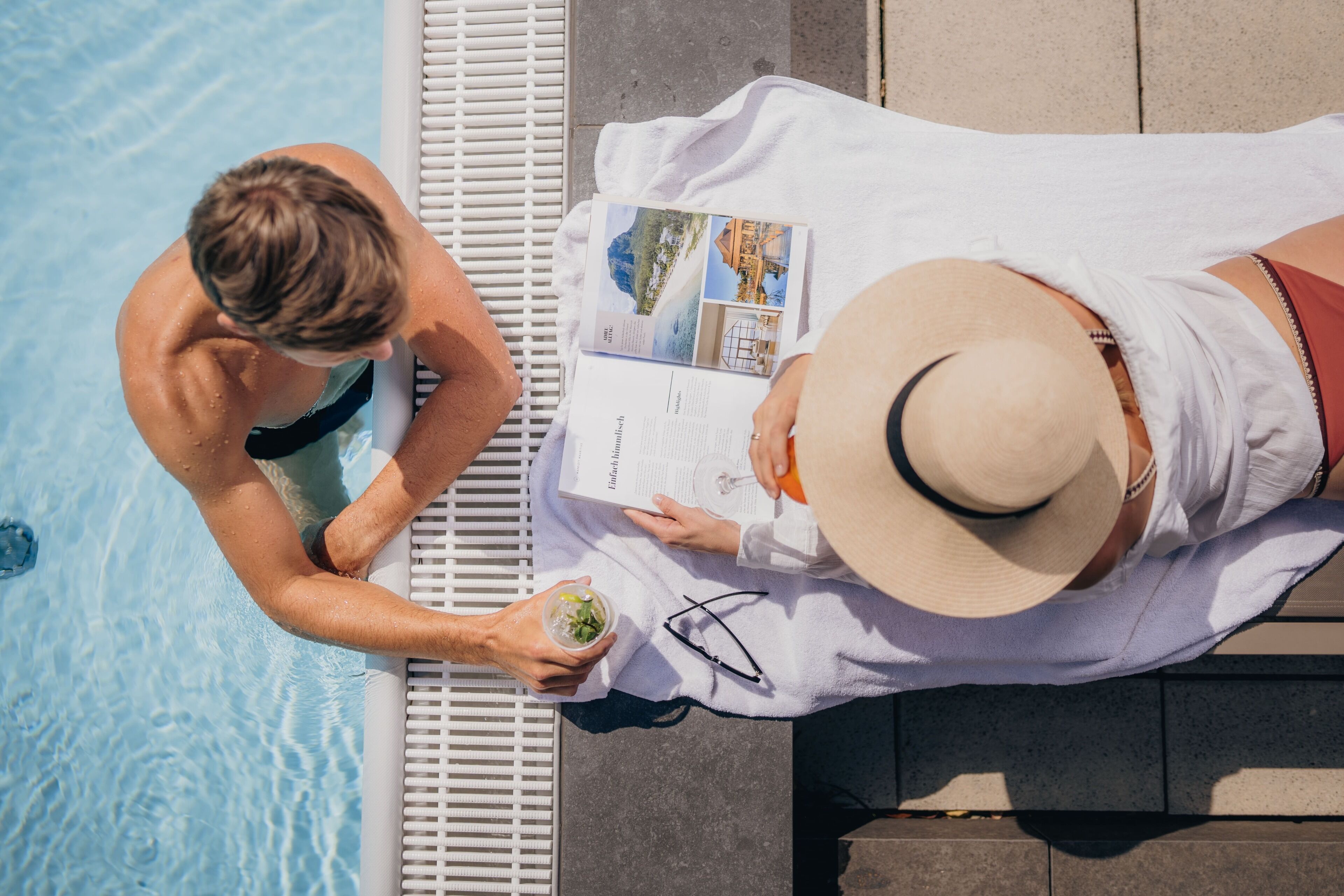 A poolside area with a lounge chair and a person reading a magazine.