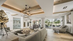 A spacious living area with a large sofa, a coffee table, and a dining table. There is a chandelier hanging from the ceiling, and a large window providing a view of the outdoors. - Jordan's Untermühle (Koengernheim)