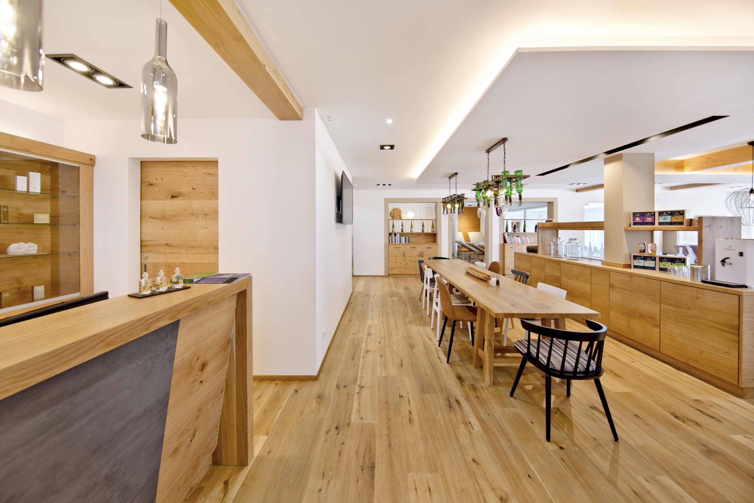 Una cocina moderna con encimeras de madera, una zona de comedor con una mesa larga y sillas, y plantas verdes colgantes.
