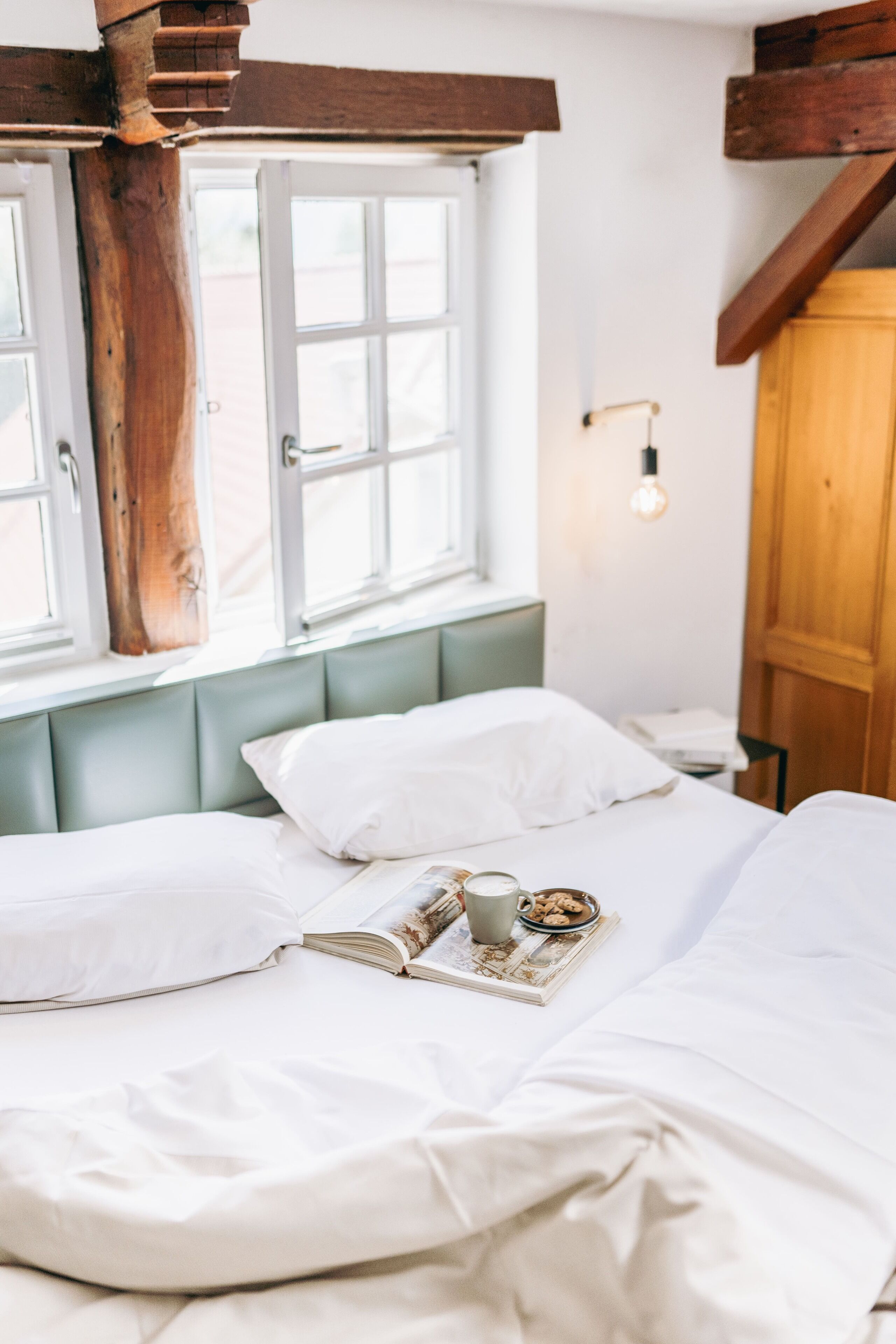 A bed with white bedding, a wooden headboard, and a window with white frames.