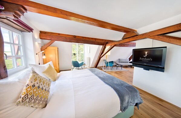 A bedroom with a large bed, a TV mounted on the wall, wooden beams, and a view of the outdoors. - Jordan's Untermühle (Koengernheim)