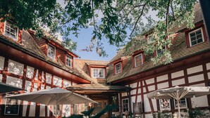 A courtyard with a traditional half-timbered building, outdoor seating, and a large umbrella. - Jordan's Untermühle (Koengernheim)