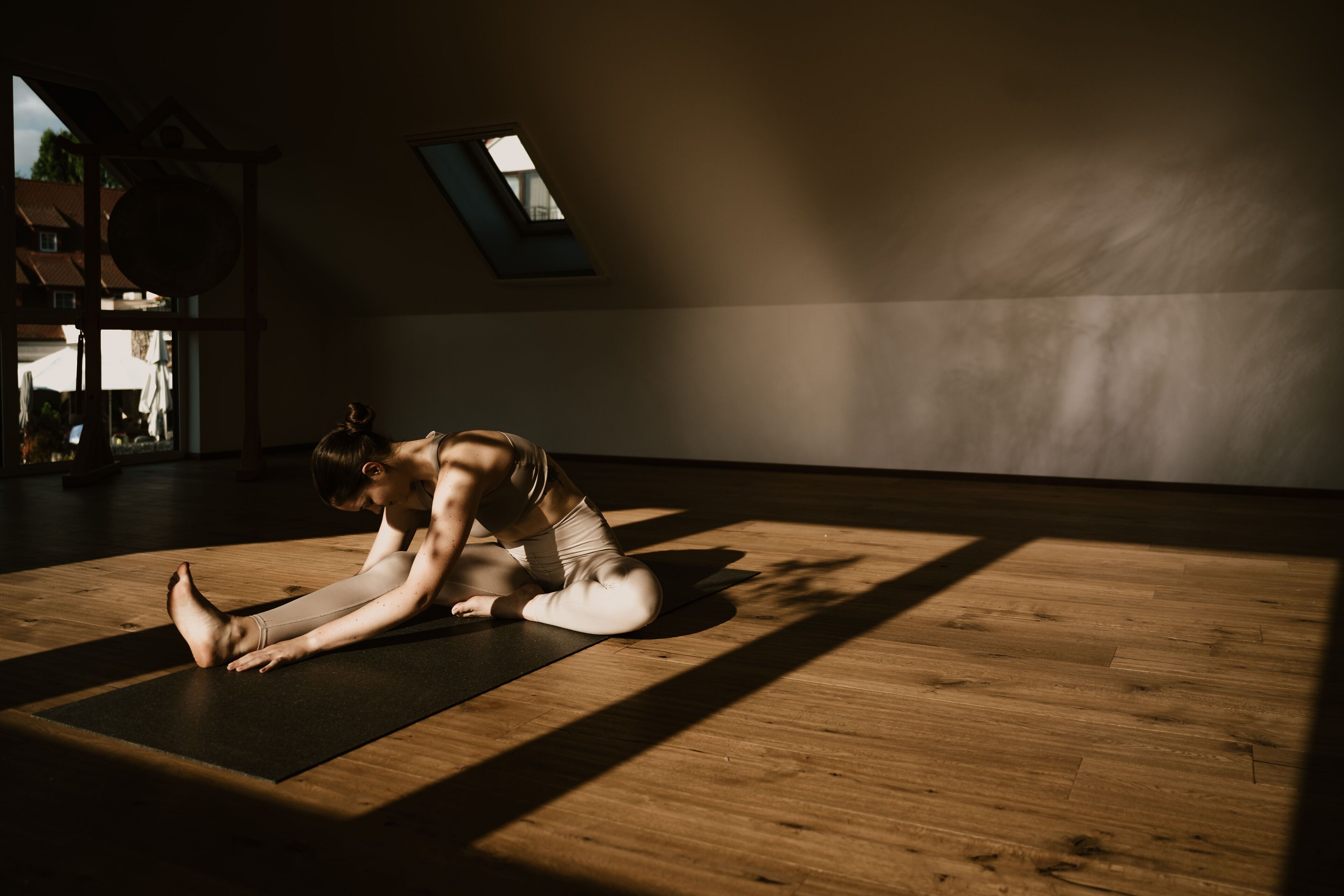 Eine Person führt eine Yoga-Pose auf einer Matte in einem Raum mit Holzboden und Dachfenstern aus.
