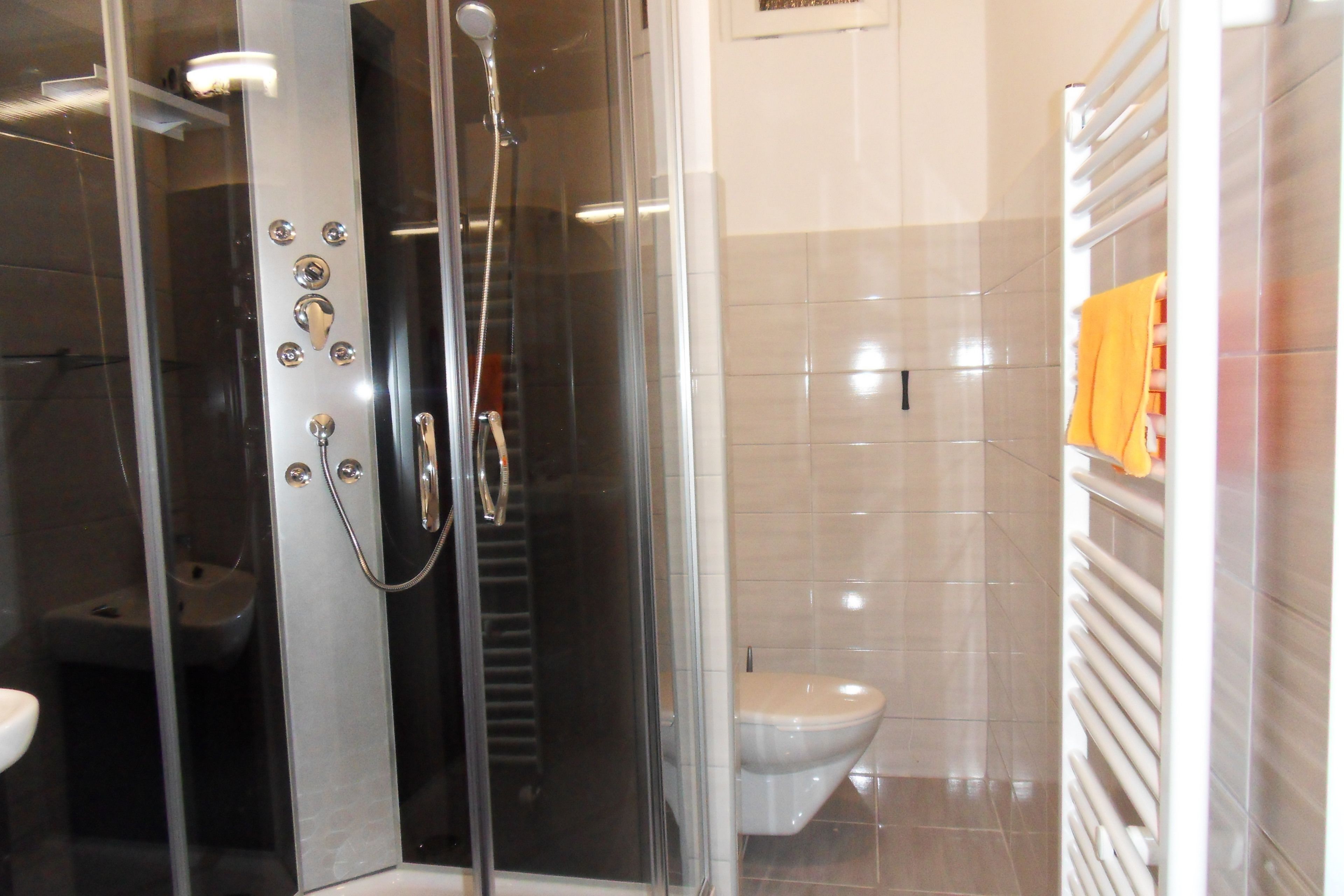 Une salle de bain avec une douche à parois de verre, des toilettes et un porte-serviettes sur lequel est posée une serviette jaune.