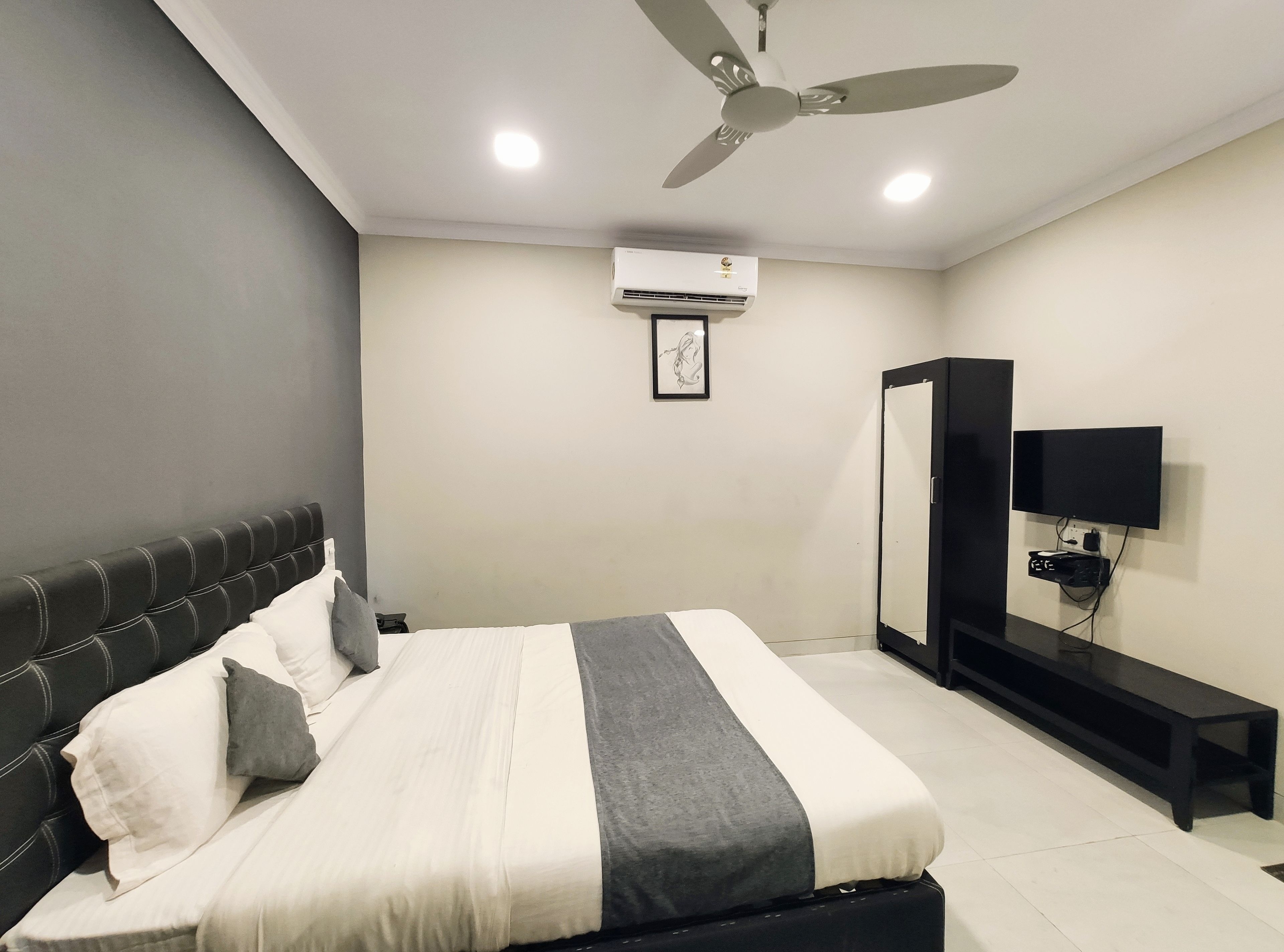 Une chambre moderne équipée d’un lit, d’un ventilateur de plafond, d’un climatiseur, d’une télévision et d’une armoire noire.