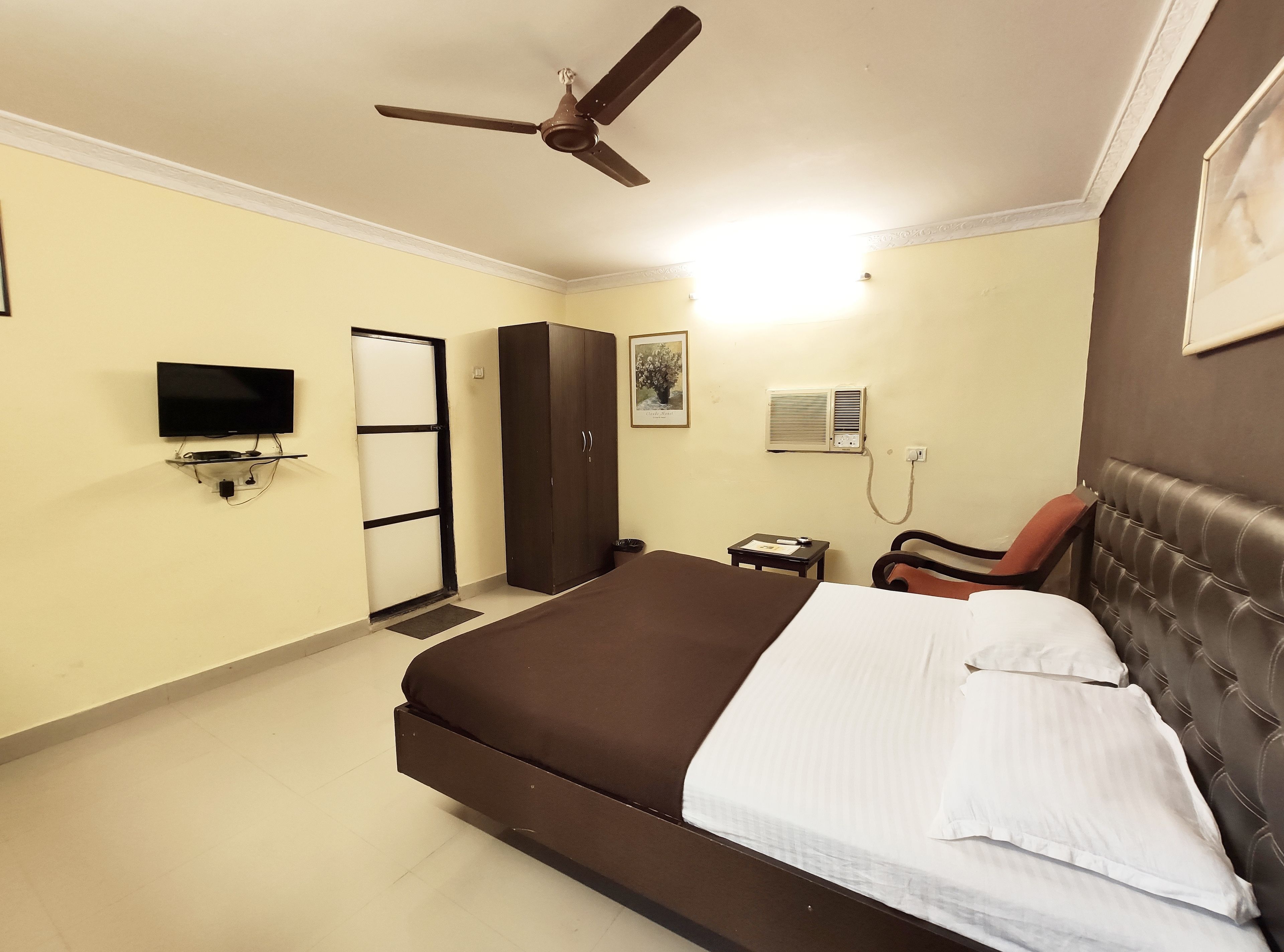 Habitación de hotel con cama, escritorio, silla, armario, televisor y aire acondicionado.