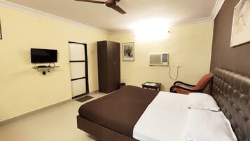 Habitación de hotel con cama, escritorio, silla, armario, televisor y aire acondicionado.