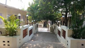 A pathway flanked by buildings with light-colored walls and red-tiled windows, leading to a central area with a door.