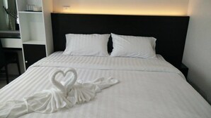 Una cama bien hecha con sábanas y almohadones blancos, y una toalla con forma de corazón sobre la cama, junto a una mesita de noche con una lámpara.