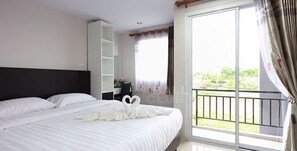 A bedroom with a large bed, a wardrobe, and a balcony with a view of greenery.