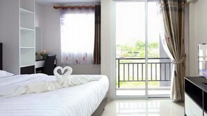 Una habitación de hotel con cama, escritorio, armario y balcón con cortinas.