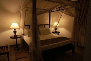 Ein schummriges Zimmer mit einem Bett unter einem Baldachin, zwei Nachttischen mit Lampen und einem kleinen Tisch ebenfalls mit einer Lampe.