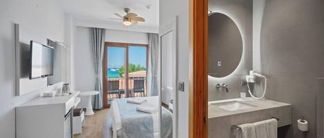 A modern hotel room with a bed, a TV, a balcony with a view, and a bathroom with a large mirror and sink.