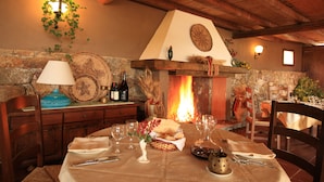A dining area with a fireplace, wooden beams, stone walls, and a table set for a meal. - Hotel Spartivento (Domus de Maria)