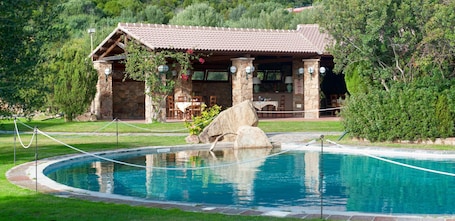 A stone building with a tiled roof, a pool with a rope barrier, and a stone wall with a rock feature.