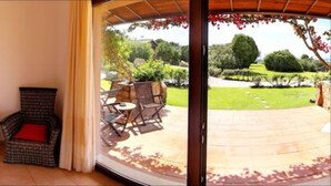 A room with a bed, a chair, and a table with chairs outside a sliding glass door. - Hotel Spartivento (Domus de Maria)