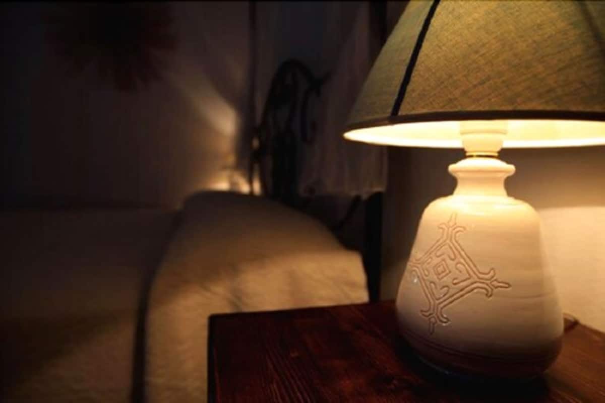 Eine Lampe mit strukturierter Lampenschirm auf einem Nachttisch aus Holz in einem schwach beleuchteten Raum.