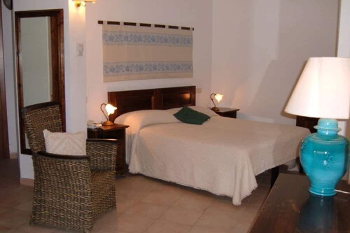 Ein Hotelzimmer mit Bett, Sessel, Nachttisch mit Lampe und Wand mit dekorativer Wandleuchte.