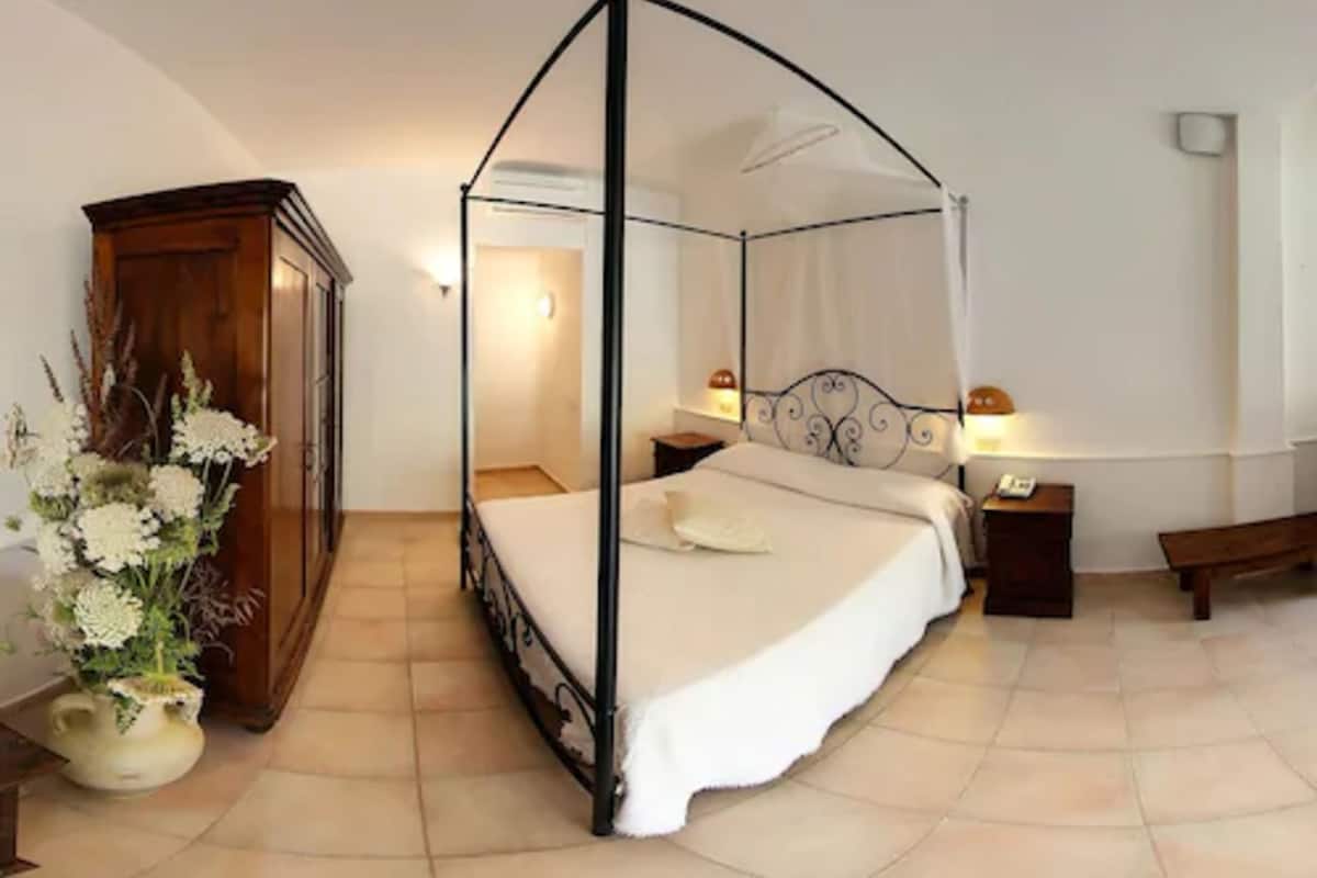 Ein Himmelsbett mit Baldachin, ein Holzschrank und ein Nachttisch mit Lampe.