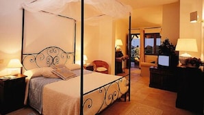 A four-poster canopy bed with a headboard, bedside tables, and a television on a stand. - Hotel Spartivento (Domus de Maria)