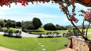 A garden with a stone wall, a pathway, and a gazebo with red flowers. - Hotel Spartivento (Domus de Maria)