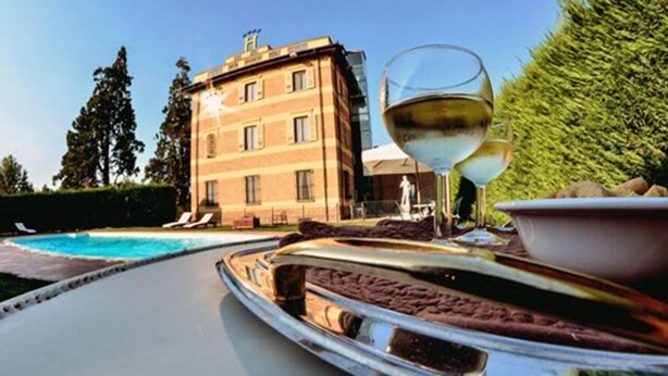 A poolside area with a glass table, a glass of white wine, and a bowl of food. - Hotel Villa Liberty (Pontecurone)