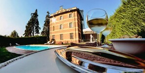 A poolside area with a glass table, a glass of white wine, and a bowl of food. - Hotel Villa Liberty (Pontecurone)