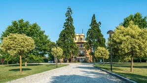 A building with a symmetrical facade, a gravel driveway, and evenly spaced trees. - Hotel Villa Liberty (Pontecurone)
