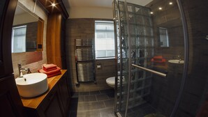 Une salle de bain moderne avec une douche à l’italienne en verre, un meuble-lavabo en bois, un lavabo blanc et une porte de douche en verre.
