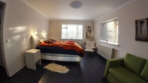 Une chambre à coucher comprenant un lit, des tables de chevet, une chaise, une fenêtre et des œuvres d’art accrochées aux murs.