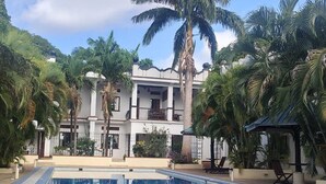 A swimming pool with a tiled deck, surrounded by palm trees and a two-story building with balconies. - Mangro Hotel Diani Beach (Ukunda)
