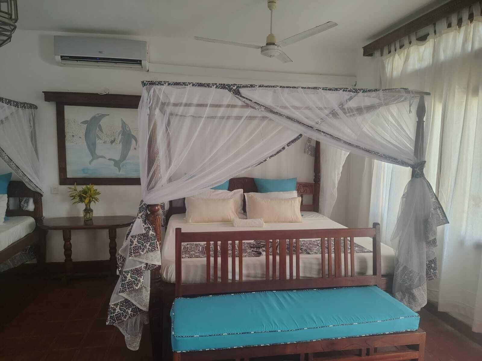 A bedroom with a four-poster bed, a ceiling fan, and a mosquito net.