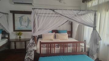 A bedroom with a four-poster bed, a ceiling fan, and a mosquito net.