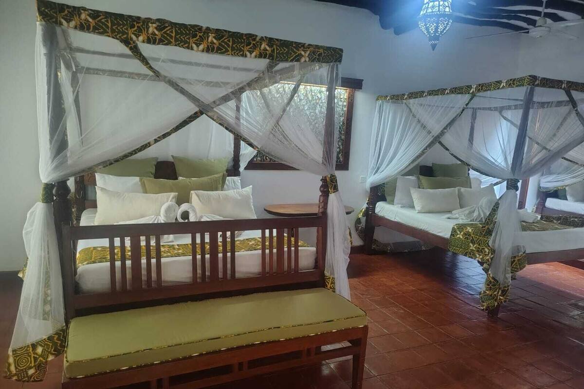 A room with a wooden bed with a canopy, a bench, and a small table.