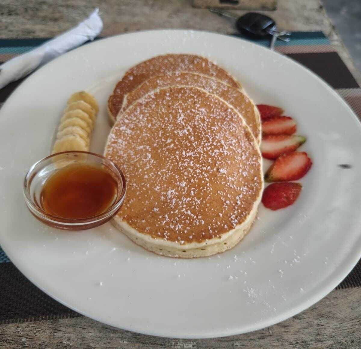 Um prato com panquecas, morangos e calda.