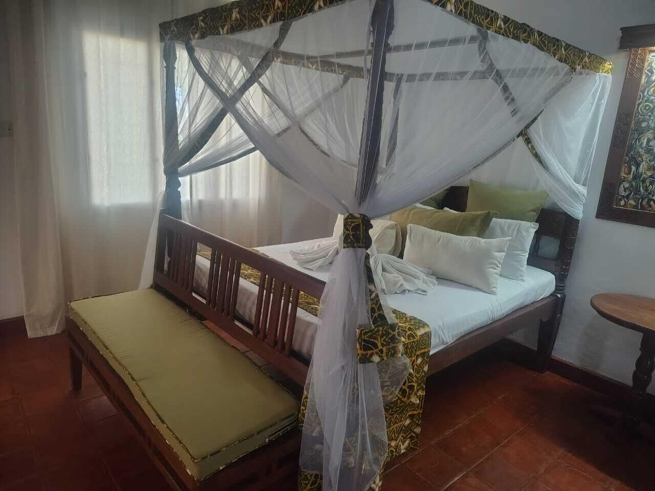 A room with a bed under a canopy, a bedside table, and a chair.