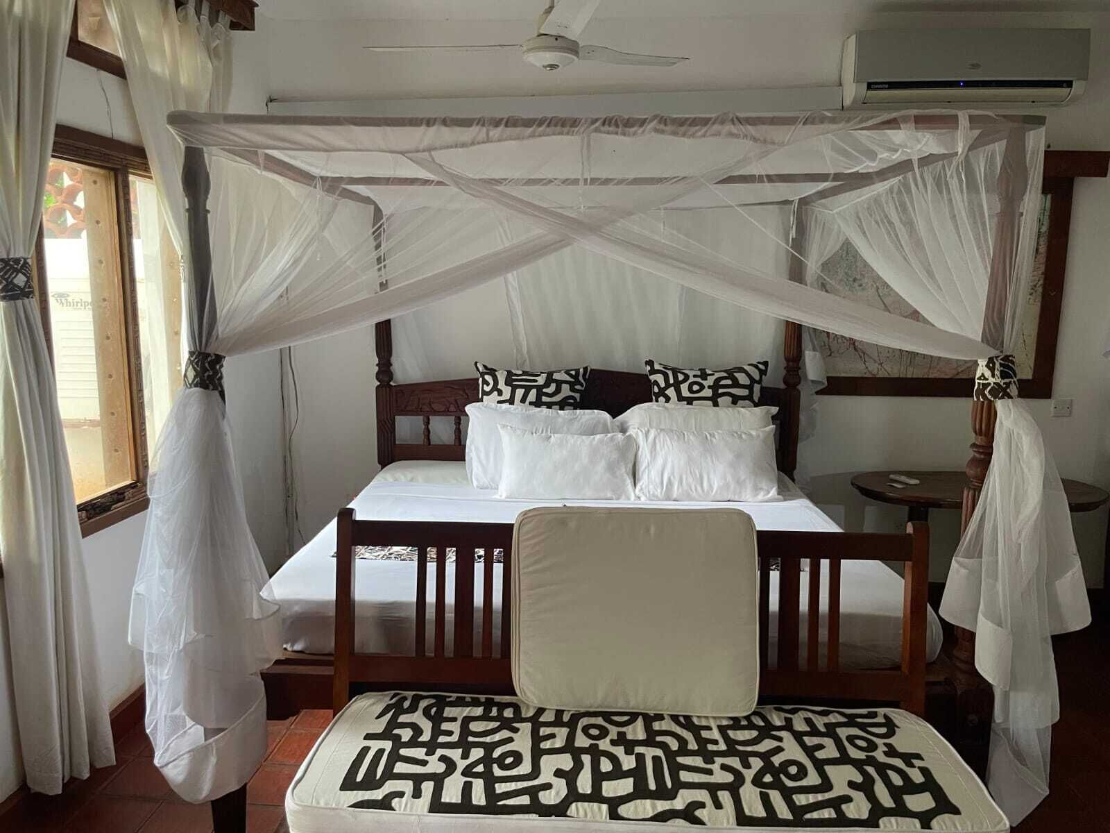 Een slaapkamer met een hemelbed, witte beddengoed en een klamboe.
