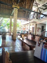 A covered outdoor seating area with stone pillars, wooden benches, and a thatched roof.