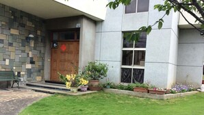 A building with a stone facade, a wooden door, and a small garden with potted plants and flowers. - Yuan Zhong Yuan B&B (Luye)
