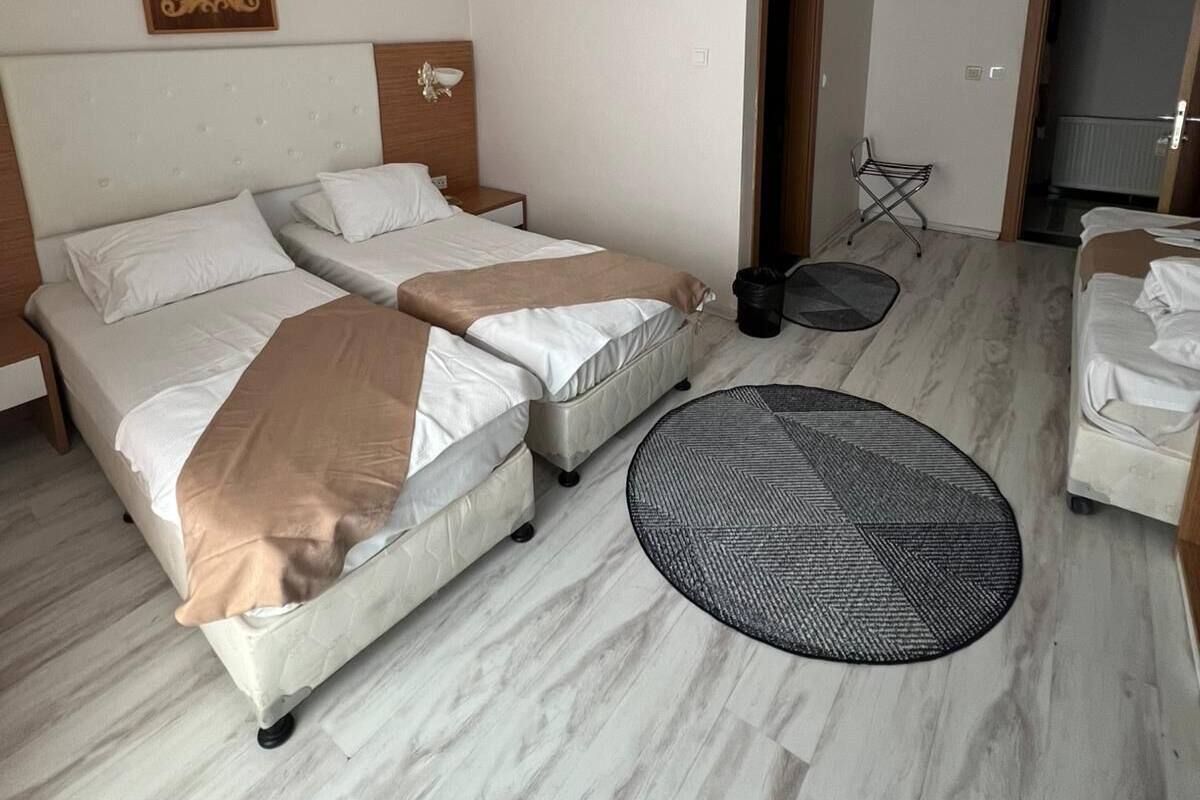 A hotel room with two beds, a round rug, a ceiling light, and a door leading to another room.